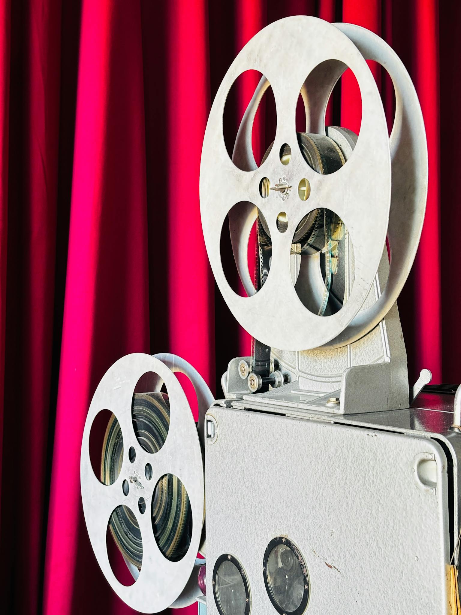 Close-up of a vintage film projector against a vibrant red curtain, capturing a classic cinema vibe.