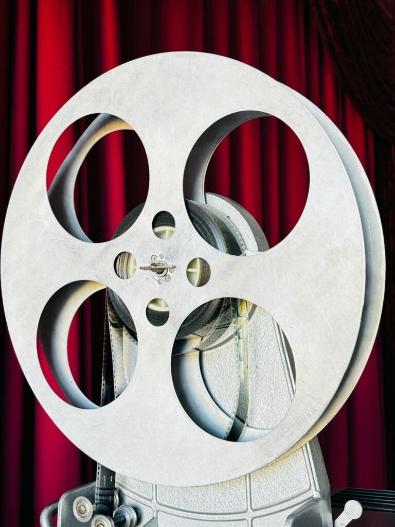 Close-up of a vintage film reel set against classic red theater curtains, evoking old cinema vibes.
