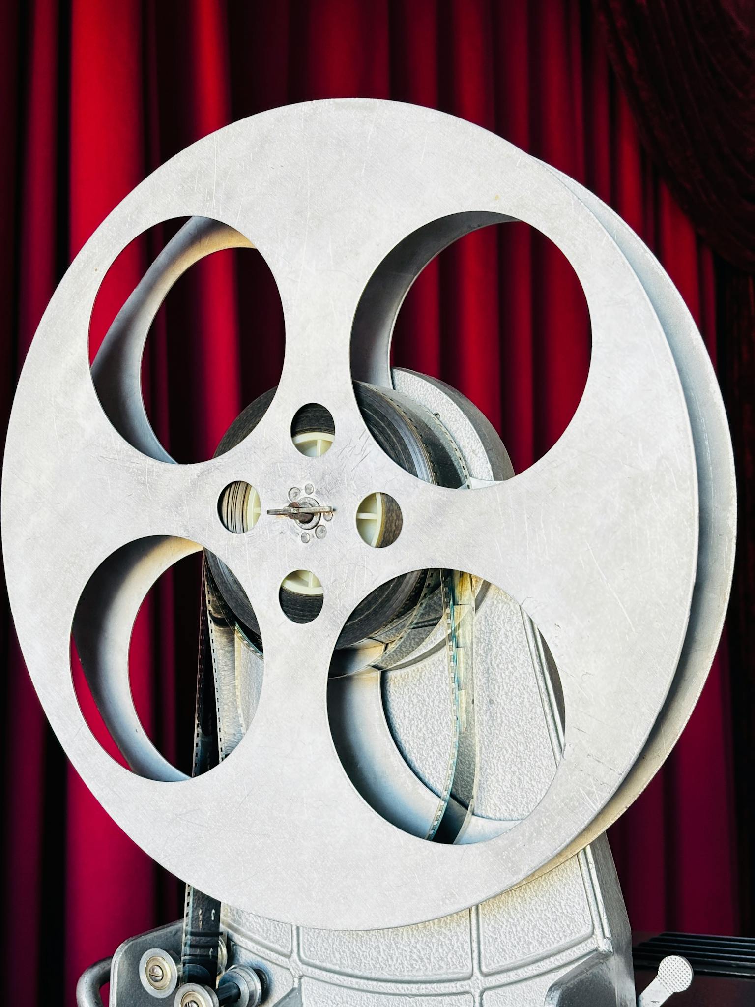 Close-up of a vintage film reel set against classic red theater curtains, evoking old cinema vibes.